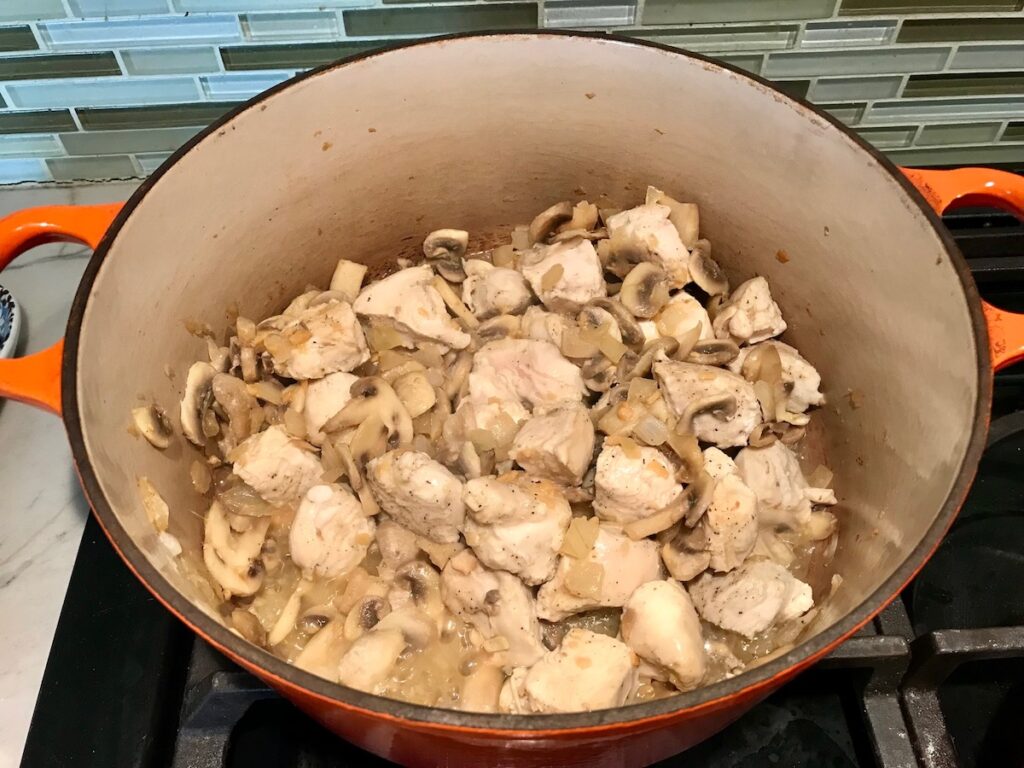 Chicken, mushrooms and onions cooking in a dutch oven for Brazilian Chicken Stroganoff.