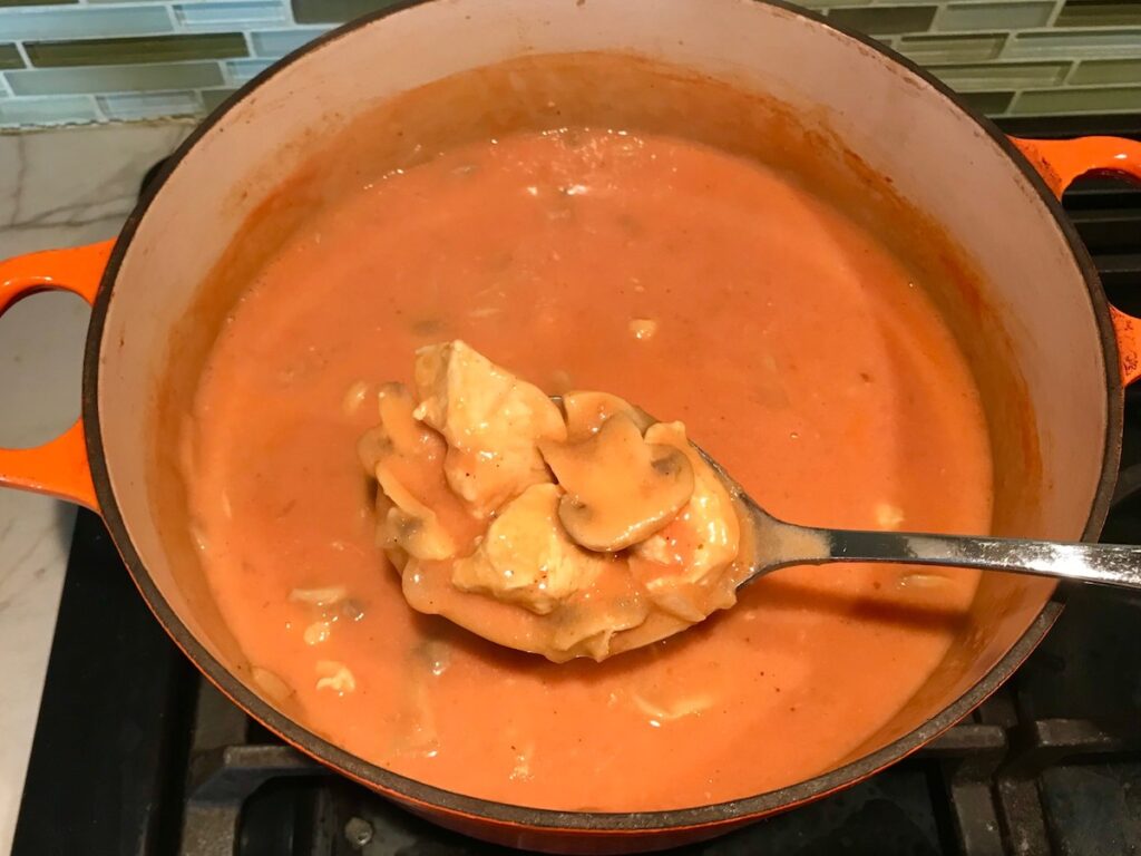 Spoon scooping cooked Brazilian Chicken Stroganoff from a dutch oven.