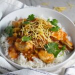 Brazilian Chicken Stroganoff in a tomato-based sauce in a bowl over white rice with cilantro garnish and thin potato sticks on top. This is an easy 30 minute dinner with a tomato based sauce, cream, and mushrooms all over rice.