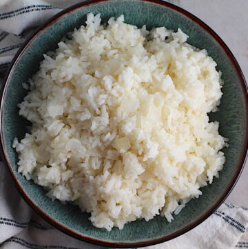 Brazilian Rice in a bowl on counter next to a towel. It's fluffy white rice flavored with sauteed garlic and onion. It takes only a couple additional steps and goes with anything!