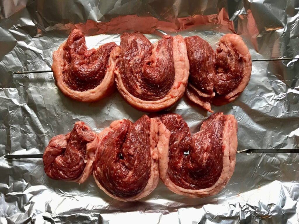 Slices of Picanha steak folded over and skewered on aluminum foil lined sheet pan for the Brazilian Steak recipe.