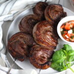 Picanha steak skewered on a plate with a tomato salad and basil leaves. It's the best Brazilian steak recipe, a tender and delicious cut of beef seasoned with a Brazilian blend and grilled perfectly!