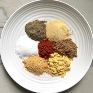 Plate with seven separate seasonings labeled to be blended into this Brazilian Steak Seasoning.