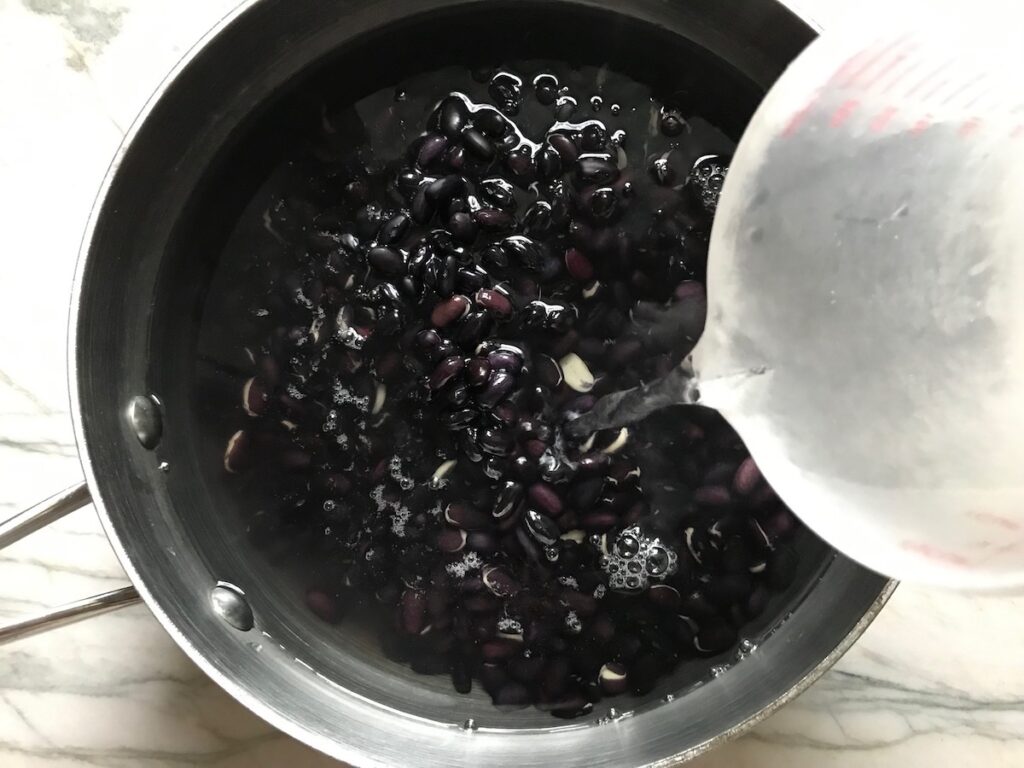Pouring water over dry black beans in a pot for Brazilian beans recipe.