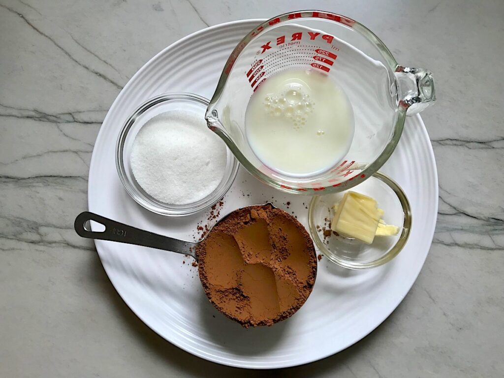 Milk, sugar, butter, and unsweetened cocoa powder measured on on a plate on counter for Brazilian Carrot Cake.