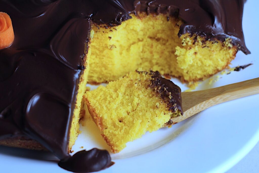 Brazilian Carrot Cake with Chocolate Sauce topping on a platter with slice missing and bamboo fork holding a bite. It's absolutely delicious and easy to make!