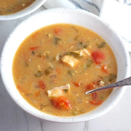 Brazilian Coconut Chicken Stew in two bowls, one with a spoon, and slow cooker in background. It's an easy family dinner. It's has chicken thighs, tomatoes, lime, cilantro, and more. Cook in a slow cooker or on the stove!