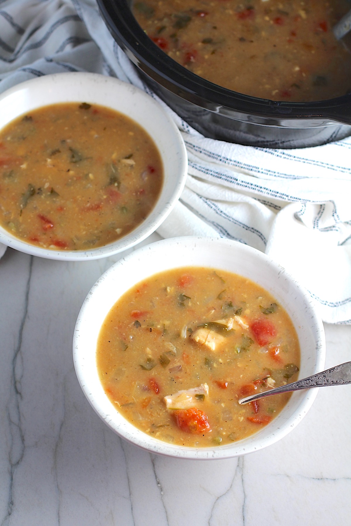 Brazilian Coconut Chicken Stew in two bowls, one with a spoon, and slow cooker in background. It's an easy family dinner. It's has chicken thighs, tomatoes, lime, cilantro, and more. Cook in a slow cooker or on the stove!