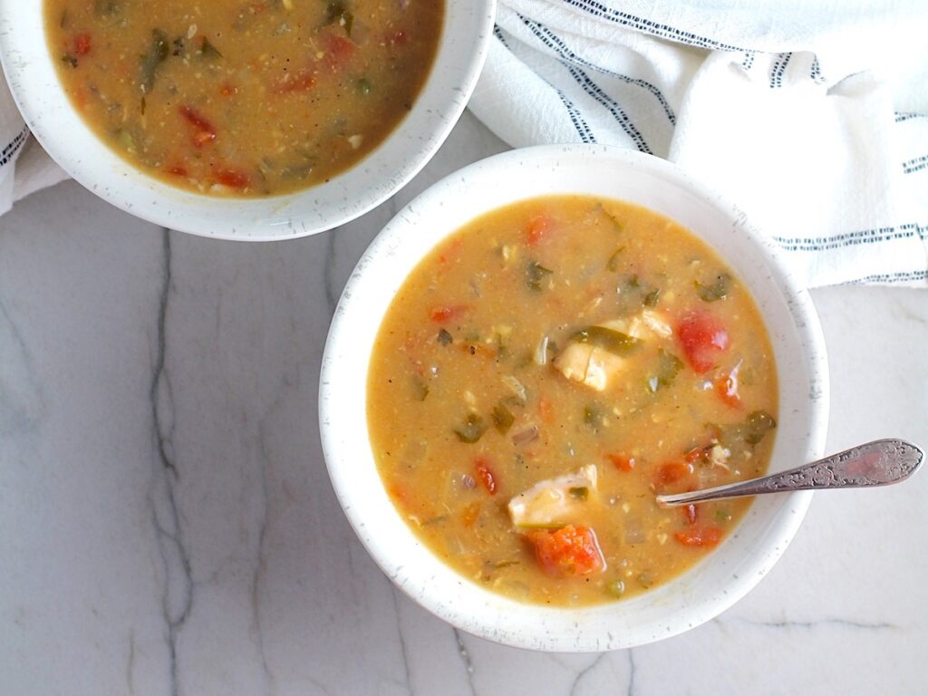 Brazilian Coconut Chicken Stew in two bowls, one with a spoon, and slow cooker in background. It's an easy family dinner. It's has chicken thighs, tomatoes, lime, cilantro, and more. Cook in a slow cooker or on the stove!