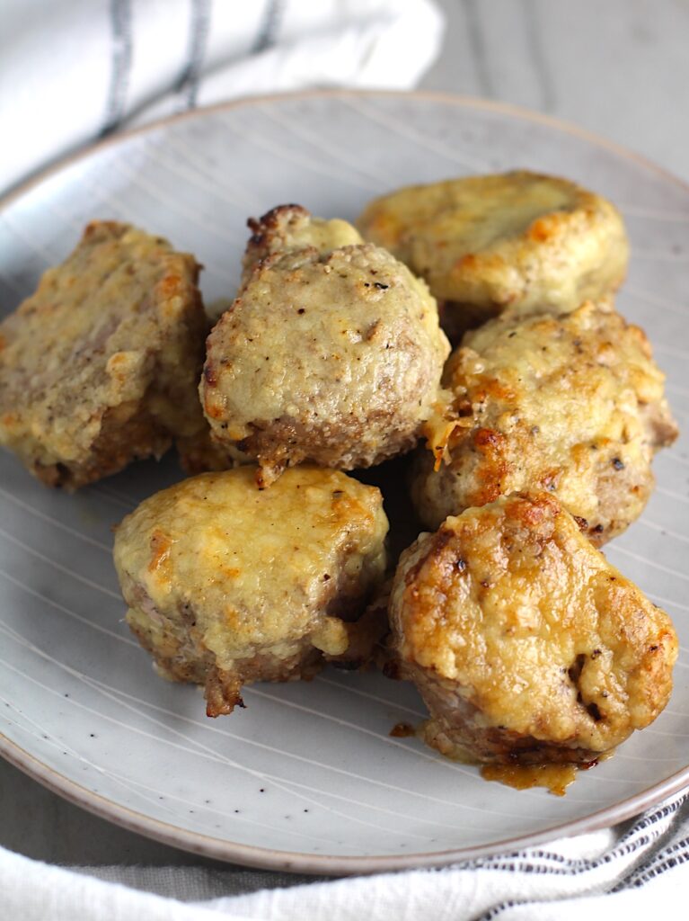 Parmesan Pork Tenderloin pieces on a plate. They are juicy, salty, and slightly cheesy. It's easy to make in the oven so you can enjoy it at home anytime!