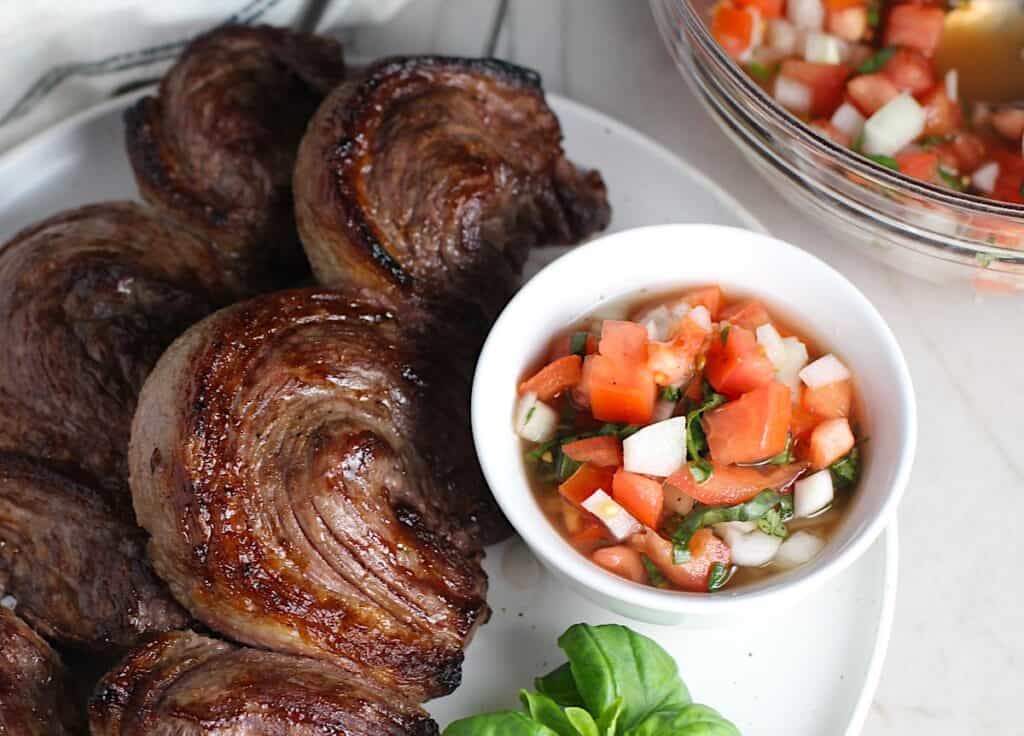 Tomato and Onion Salad in a bowl next to Picanha skewered steaks.