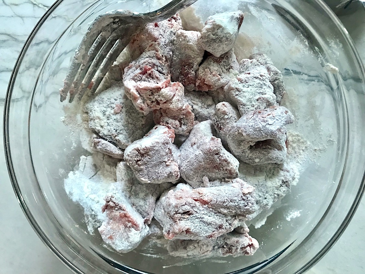 Raw beef cubes coated in flour in a bowl for Brazilian Beef Stew Stove Top recipe.