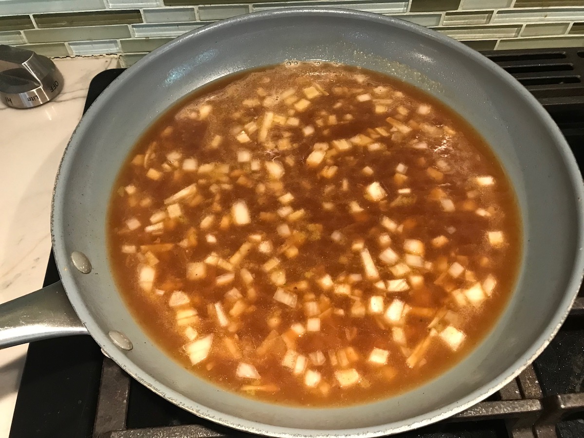 Onions and broth in skillet on stove for Brazilian Chicken in peanut sauce recipe.