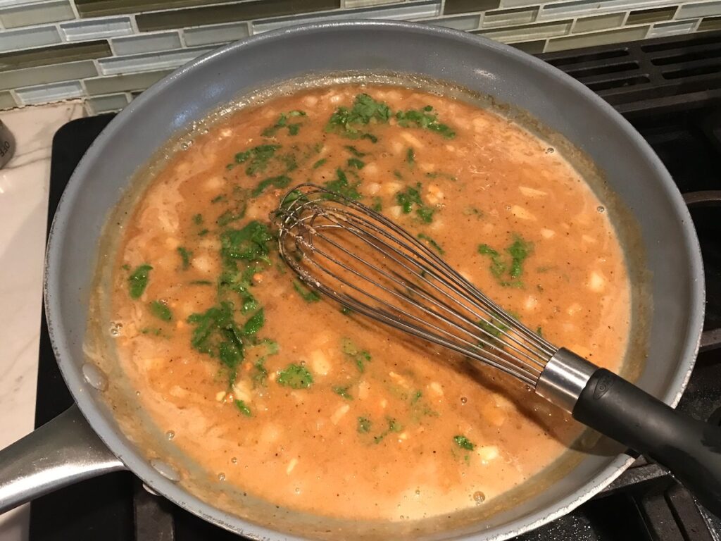 Whisk mixing in fresh cilantro into peanut sauce in skillet on stove for Brazilian Chicken recipe.