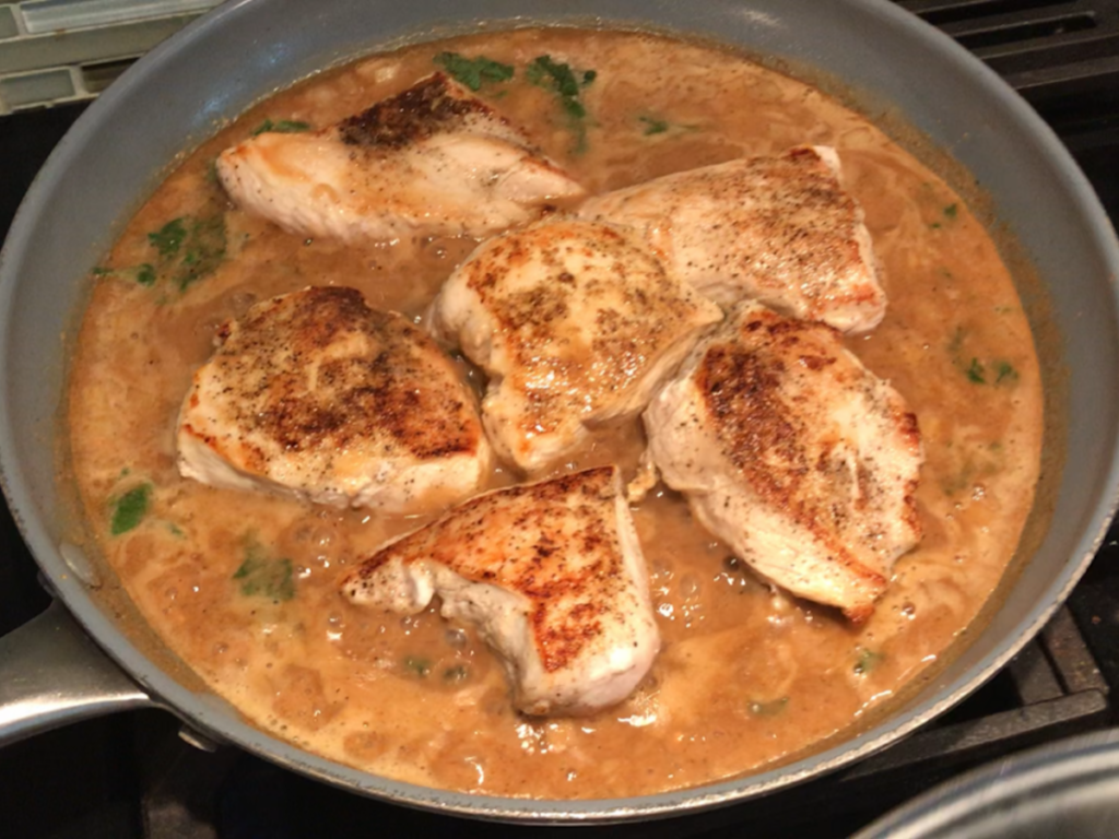 6 pieces of Brazilian Chicken sitting on top of Peanut Sauce in a skillet on stove.