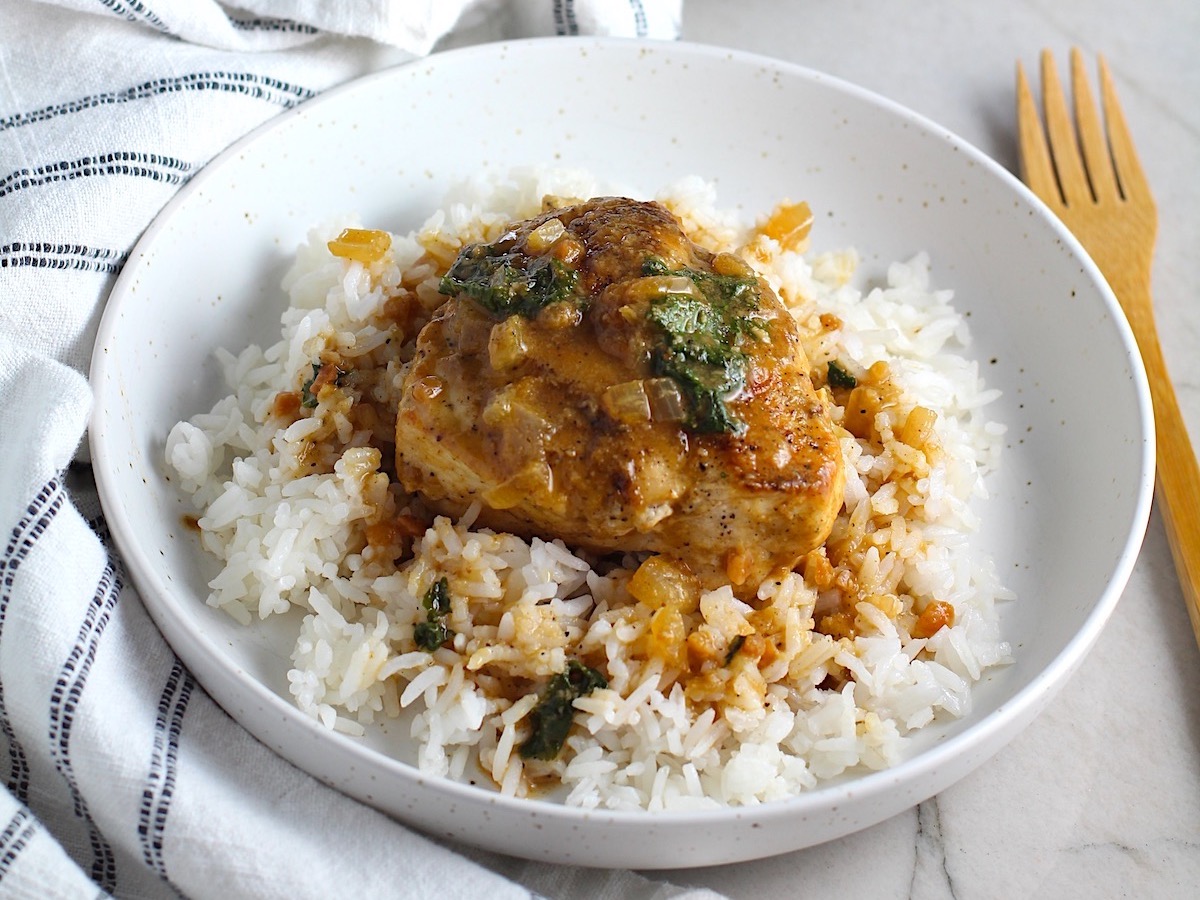 Piece of Brazilian Chicken in Peanut Sauce on top of rice on a plate on counter with dish towel next to it.