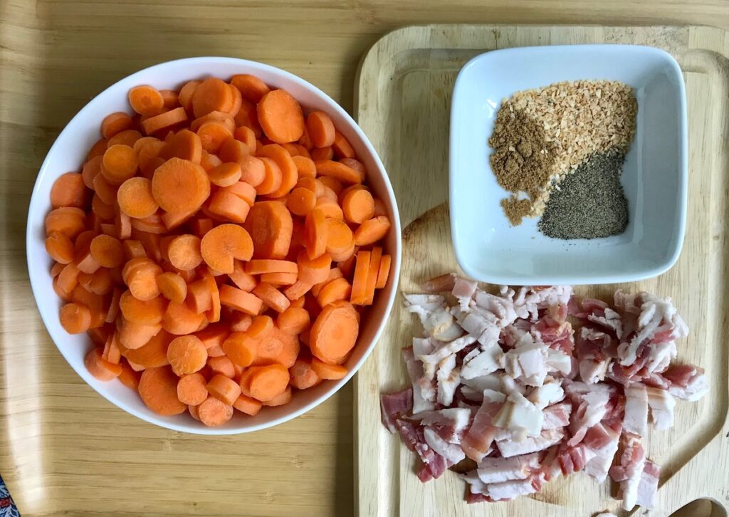 Carrots sliced in a bowl, raw bacon sliced on cutting board, and seasonings measured out in small bowl for this Carrot Bacon Recipe.