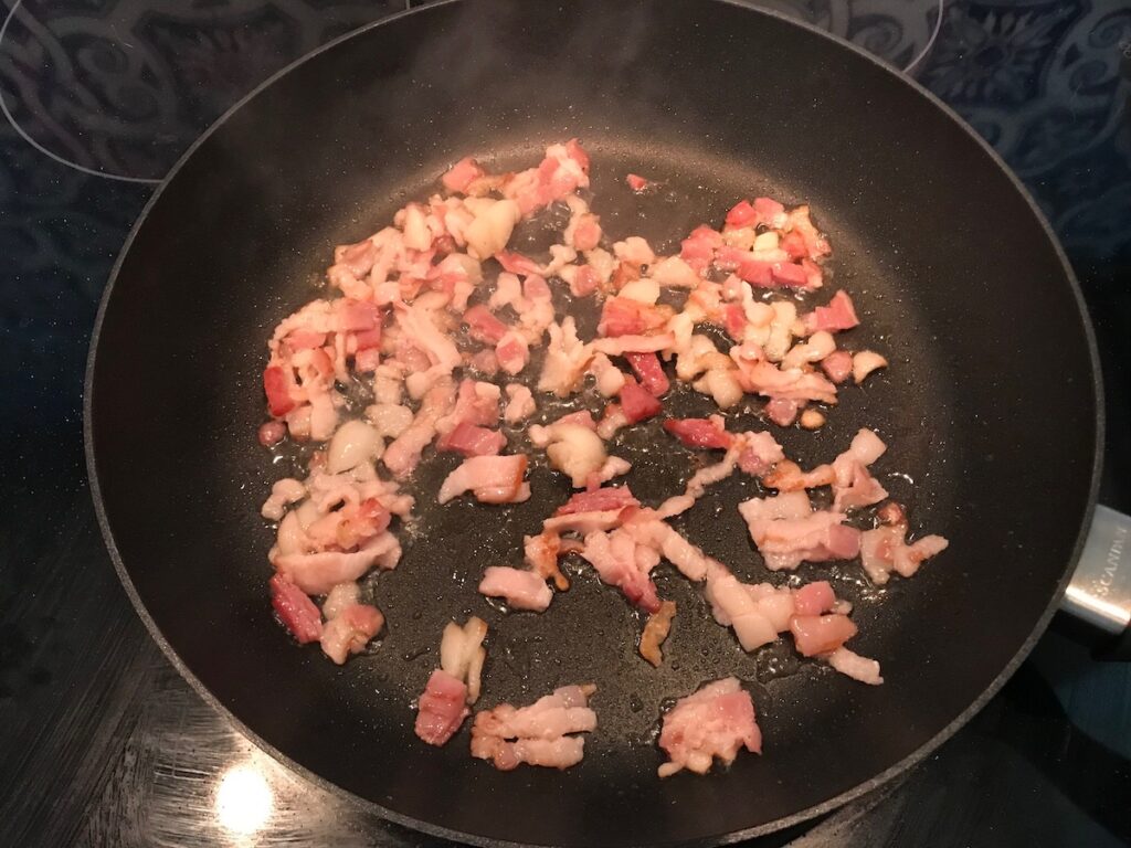 Sliced bacon cooking in a skillet for this Carrot Bacon Recipe.