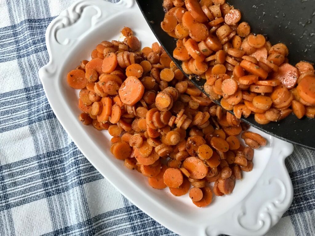 Pouring cooked Carrots and bacon from skillet to a platter for this Carrot Bacon Recipe.