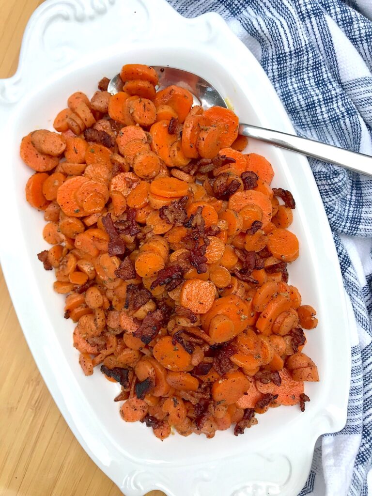 Carrot Bacon recipe on white serving platter with spoon in upper right corner and towel on table.
