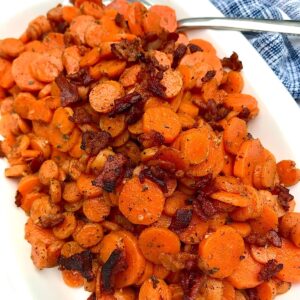 Carrot Bacon recipe on white serving platter with spoon in upper right corner and towel on table.