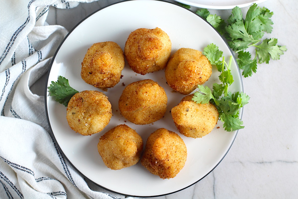Golden brown breaded Brazilian Coxinha Chicken Croquettes on a plate with cilantro garnish on a counter with towel next to it.