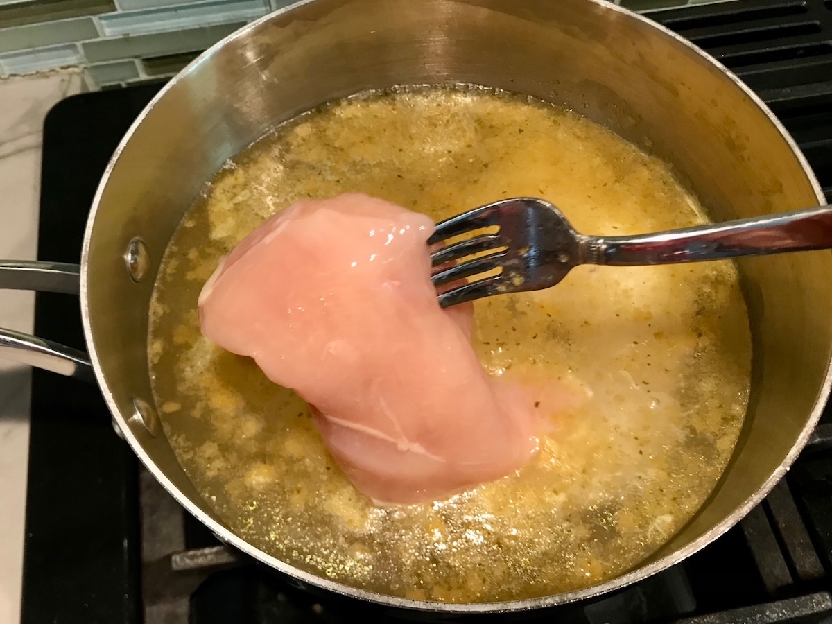 Fork adding raw chicken breast to chicken broth for Coxinha Chicken Croquettes.