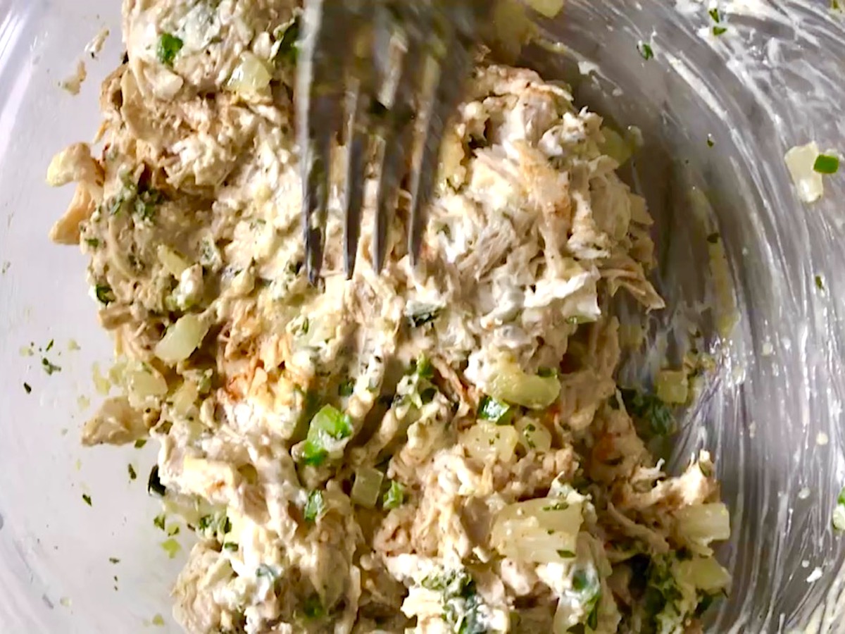 Mixed shredded chicken and cheese filling in a bowl with fork for Coxinha Chicken Croquettes.