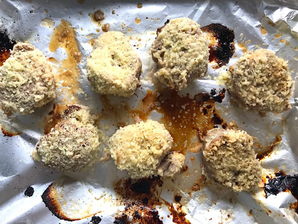 Parmesan Pork Tenderloin pieces on a pan before the parmesan is cooked on it. They are juicy, salty, and slightly cheesy. It's easy to make in the oven so you can enjoy it at home anytime!