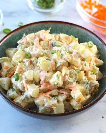 Brazilian Potato Salad in a bowl with carrots, green olives, cilantro, and a mayonnaise dressing, and cilantro garnish on top.