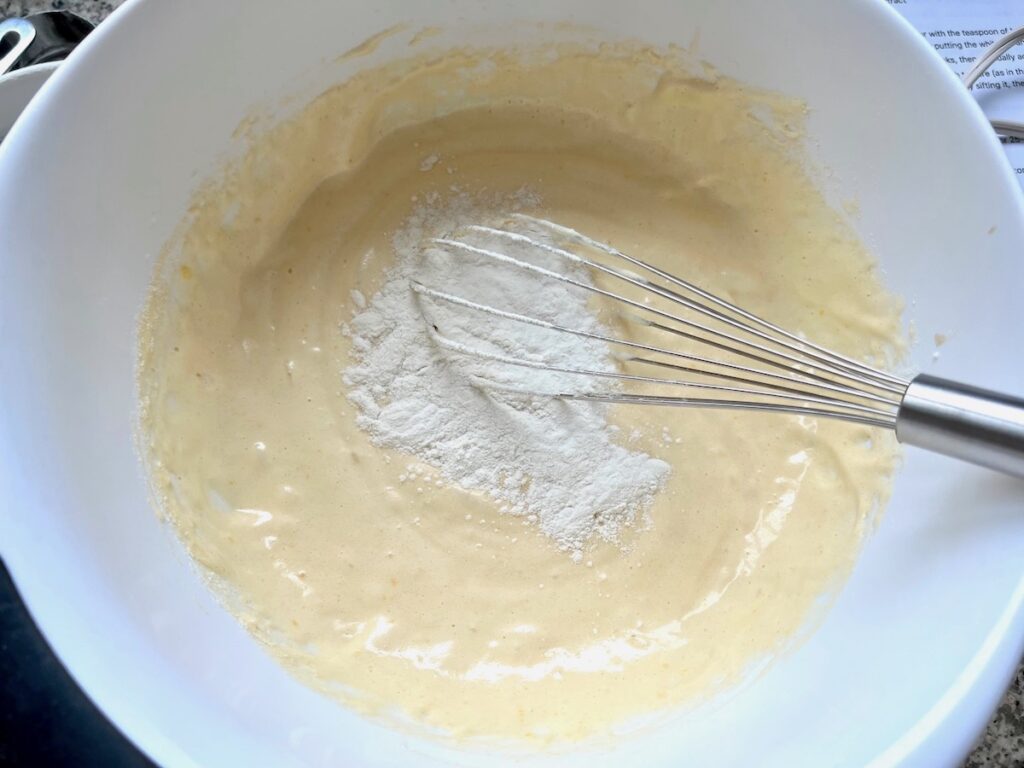 Sifted flour being whisked into batter for Brazilian Coconut Cake.