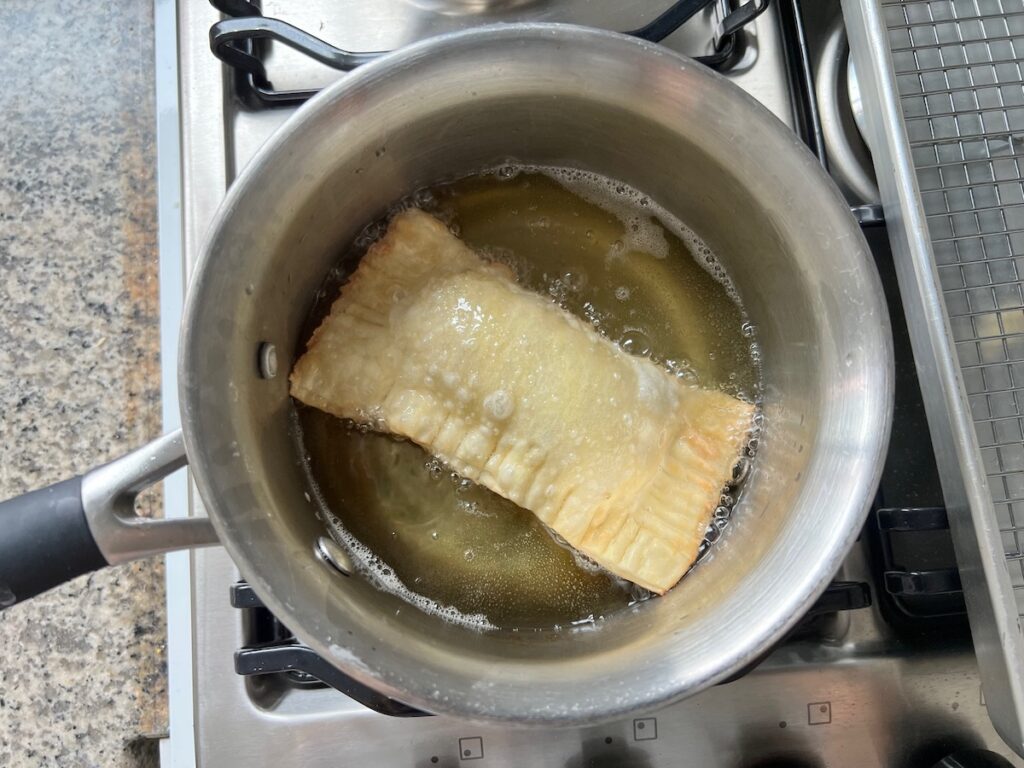 One rectangle pastel frying in a pot of oil on the stove for Brazilian Pastel recipe.