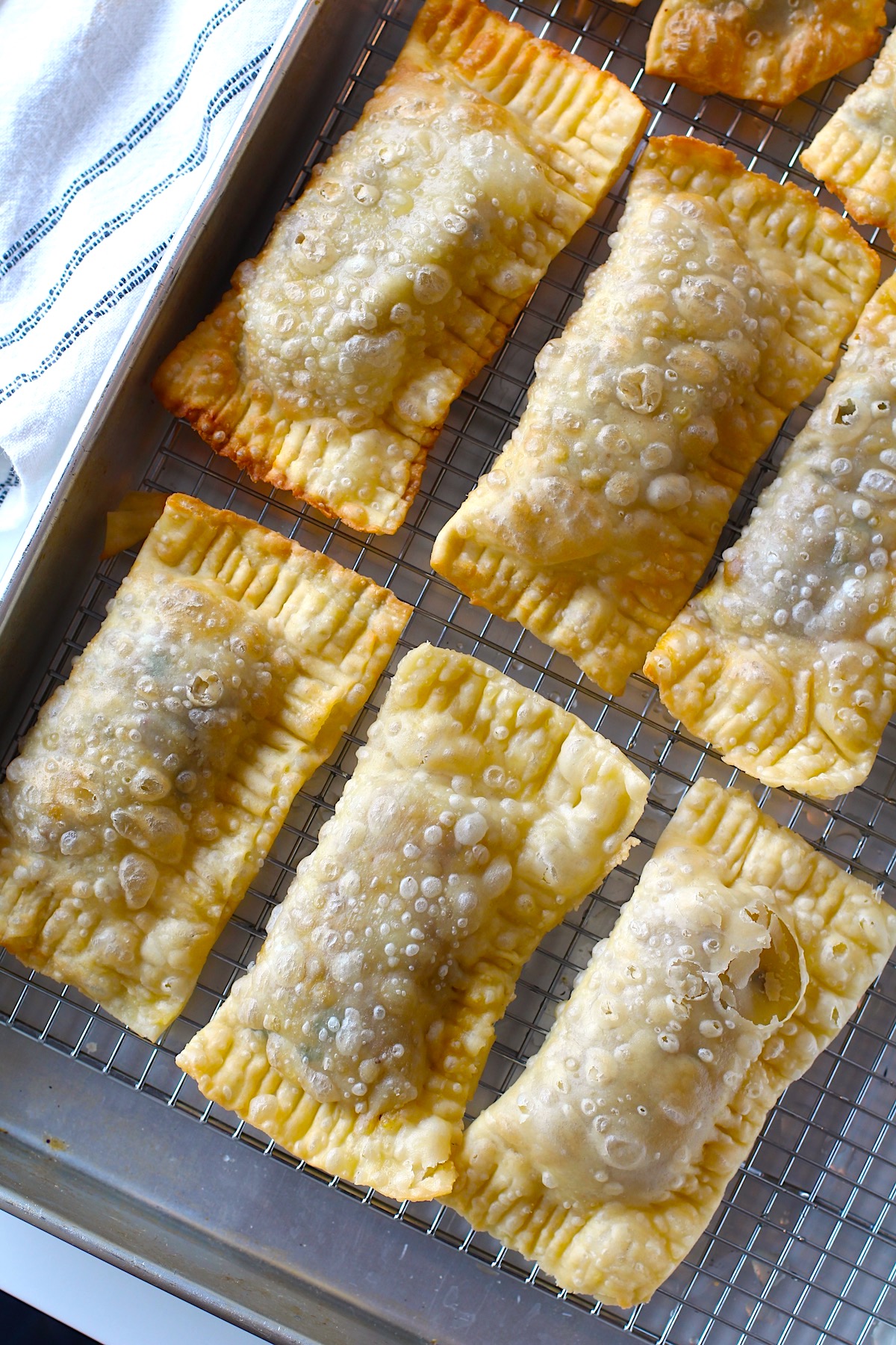 Six golden brown fried Pasteis on rack over sheet pan for traditional Brazilian Pastel Recipe with ground beef filling.