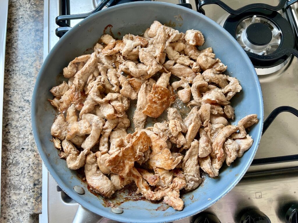 Cooked chicken strips in a skillet on stove for Marinated Chicken Stir Fry recipe. 