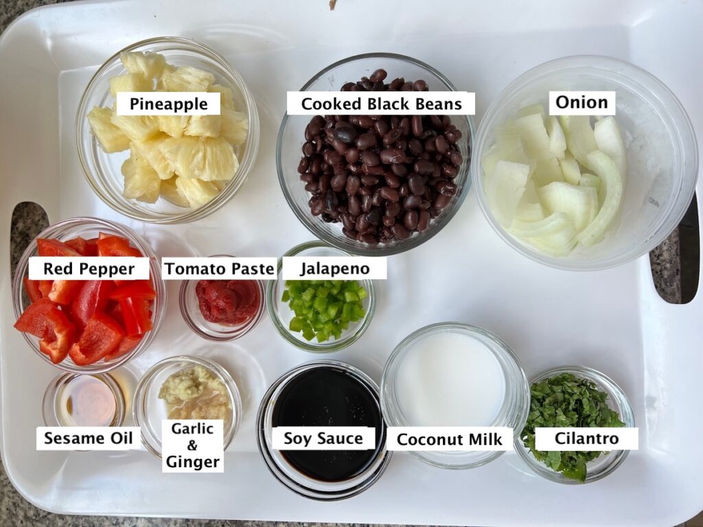 Ingredients prepped and measured out in small bowls for Brazilian Marinated Chicken Stir Fry. From top left: Diced pineapple, cooked black beans, sliced onions, chopped red pepper, tomato paste, diced jalapeno, sesame oil, minced garlic and ginger, soy sauce, coconut milk, chopped cilantro.