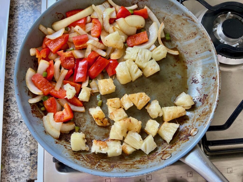 Red pepper and onions cooking on one side of pan and the pineapple chunks on the other side for Marinated Chicken Stir Fry.