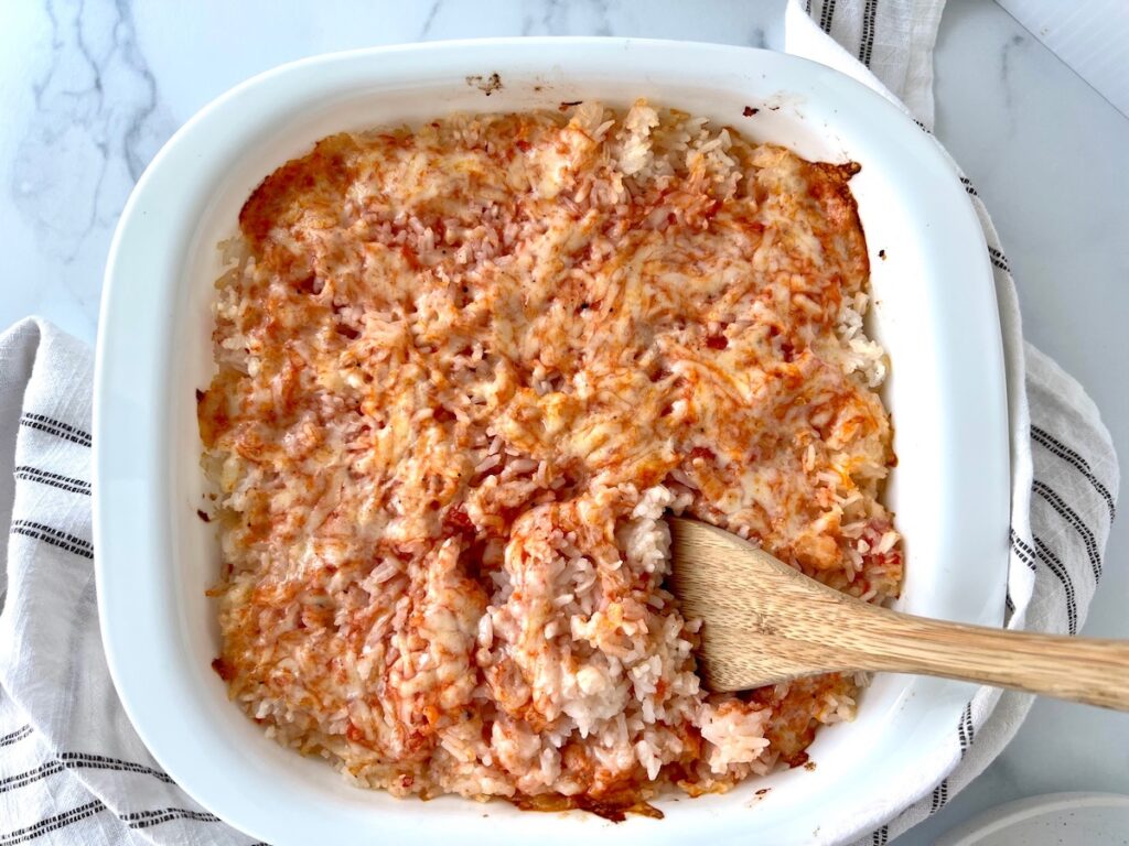 Spatula scooping Baked Rice with Cheese and Tomatoes up from casserole dish.