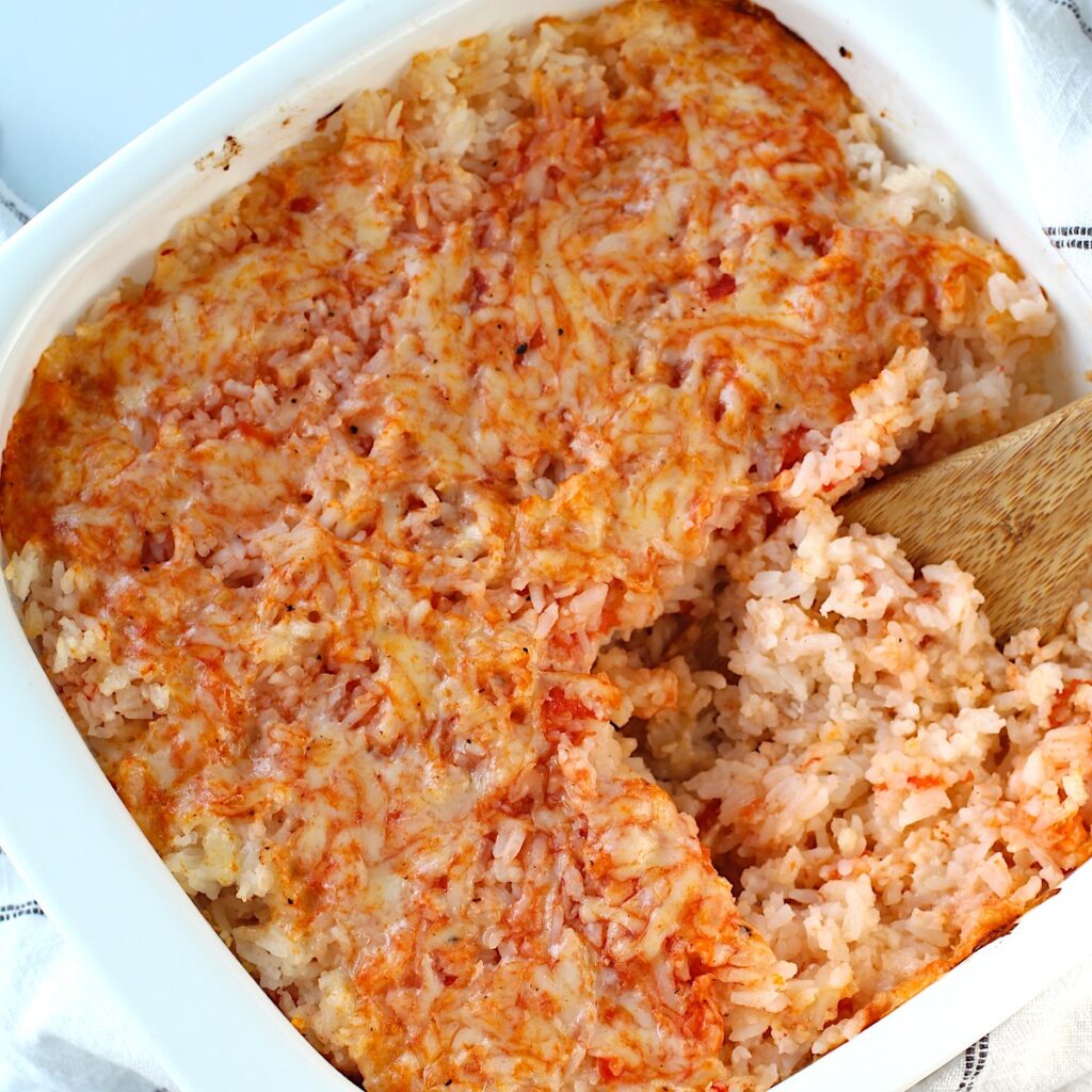 Spatula scooping Baked Rice with Cheese and Tomatoes up from casserole dish.