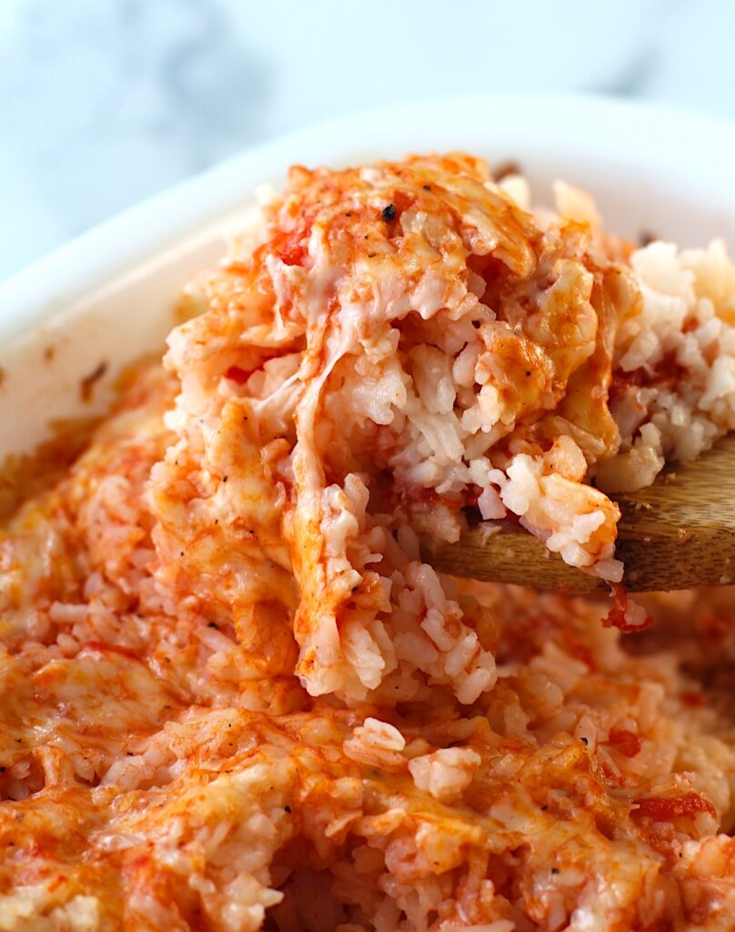 Spatula scooping Baked Rice with Cheese and Tomatoes up from casserole dish.