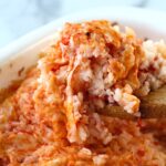 Spatula scooping Baked Rice with Cheese and Tomatoes up from casserole dish.