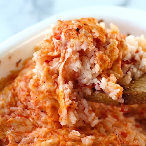 Spatula scooping Baked Rice with Cheese and Tomatoes up from casserole dish.