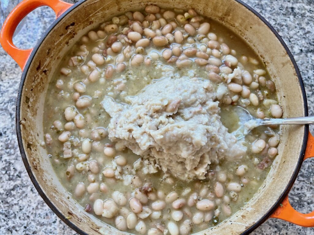 Pot of cooked carioca beans with some pureed beans being mixed in..