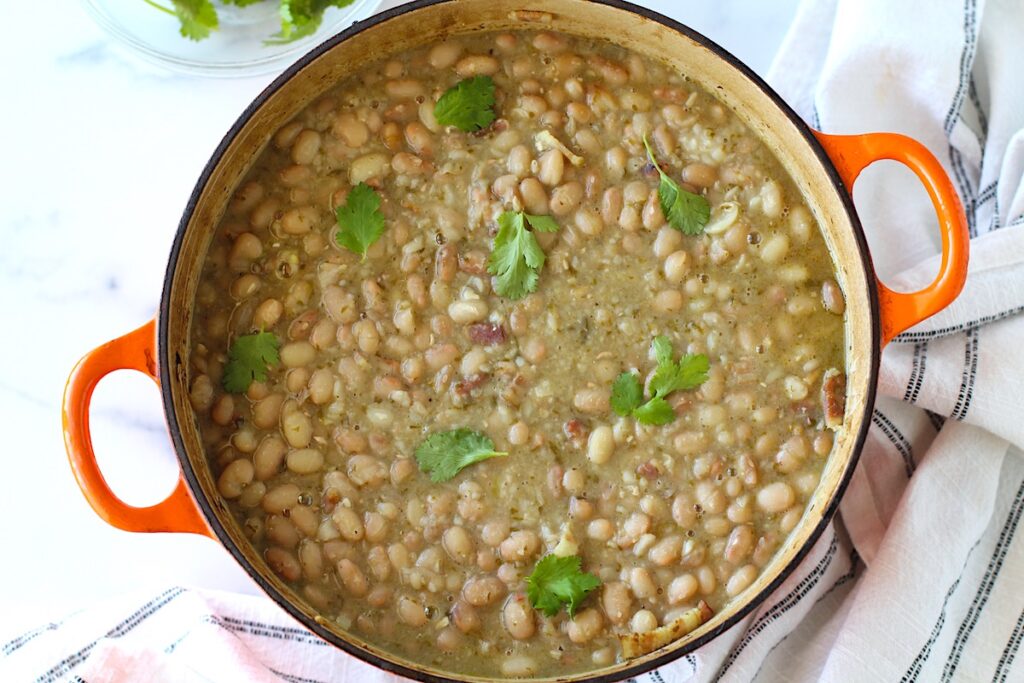 Carioca beans in a pot on the counter with towel next to it and cilantro leaves on top.