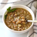 Spoon scooping up Carioca beans from a bowl of beans with cilantro leaves on top.