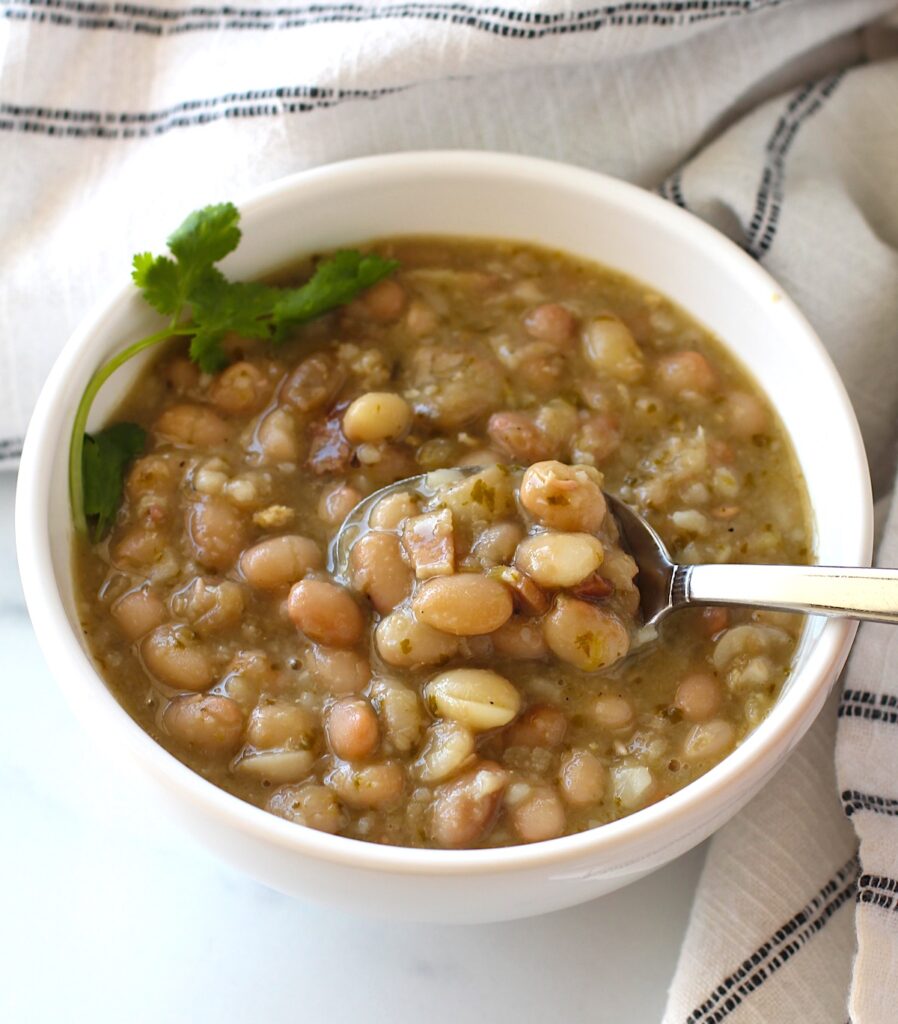 Spoon scooping up Carioca beans from a bowl of beans with cilantro leaves on top.