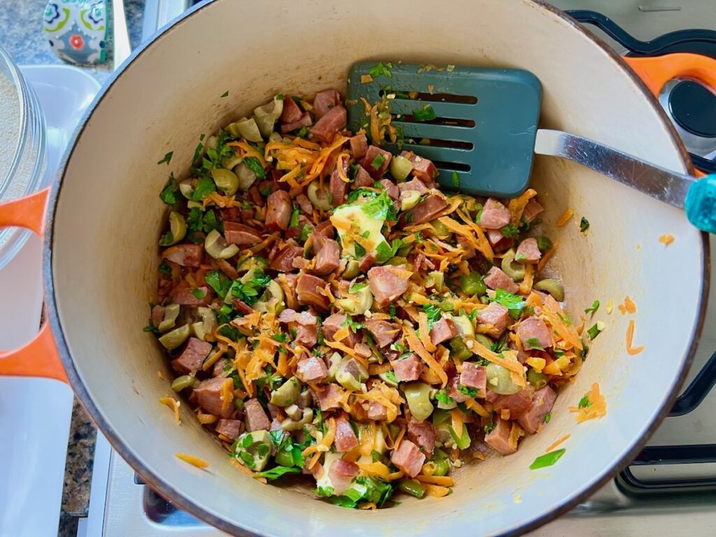 Cilantro, bacon, olives, and butter added to carrots, garlic, sausage, and scallions added to pan for Brazilian Farofa Recipe.