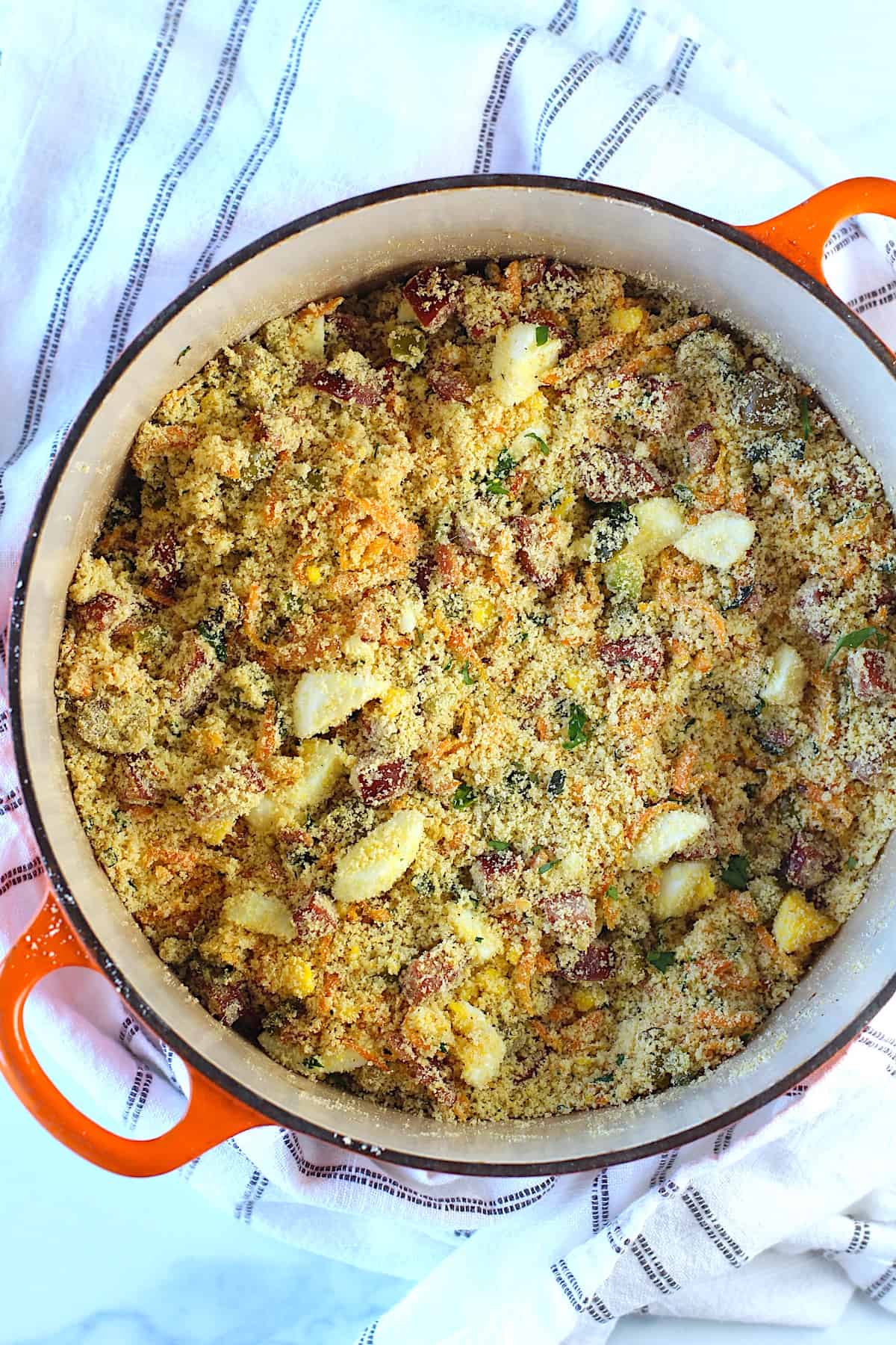 Brazilian Farofa Recipe in a pot on blue and white towel on counter.  It has bacon, sausage, green olives, hard boiled eggs, carrots, onions, and garlic and is a delicious traditional recipe for Christmas ~ Farofa de Natal.  