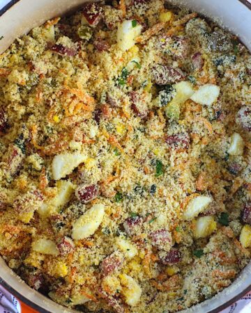 Brazilian Farofa Recipe in a pot on blue and white towel on counter. It has bacon, sausage, green olives, hard boiled eggs, carrots, onions, and garlic and is a delicious traditional recipe for Christmas ~ Farofa de Natal.