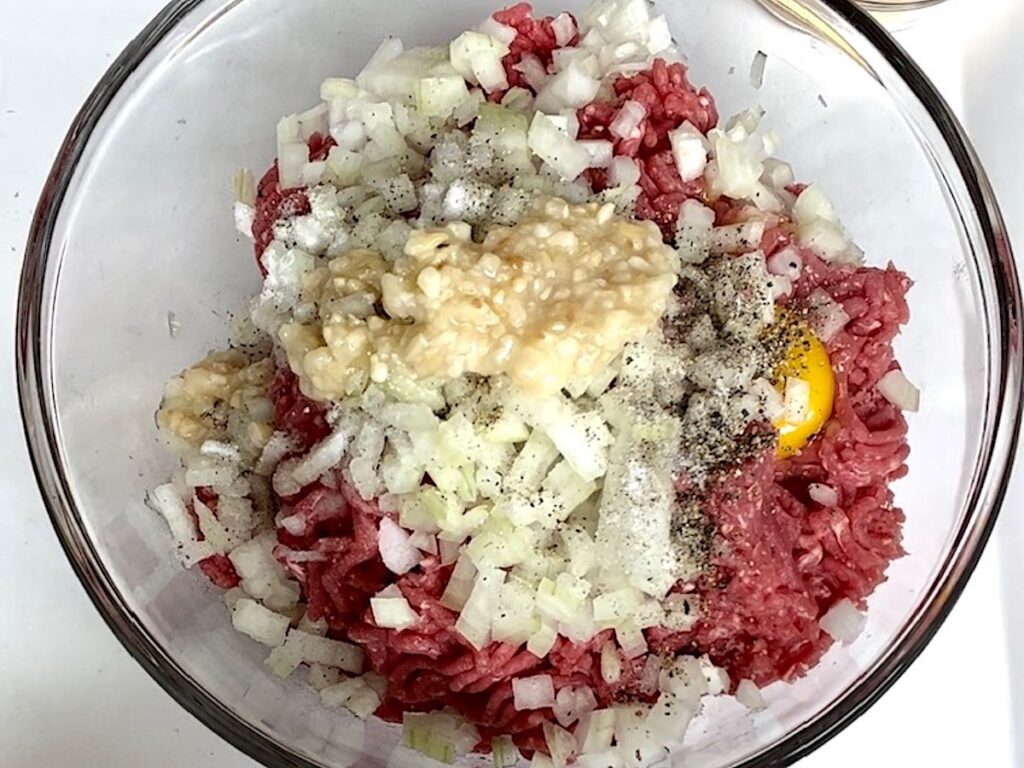Ground beef, onions, eggs, garlic, salt, pepper in a bowl before being mixed.