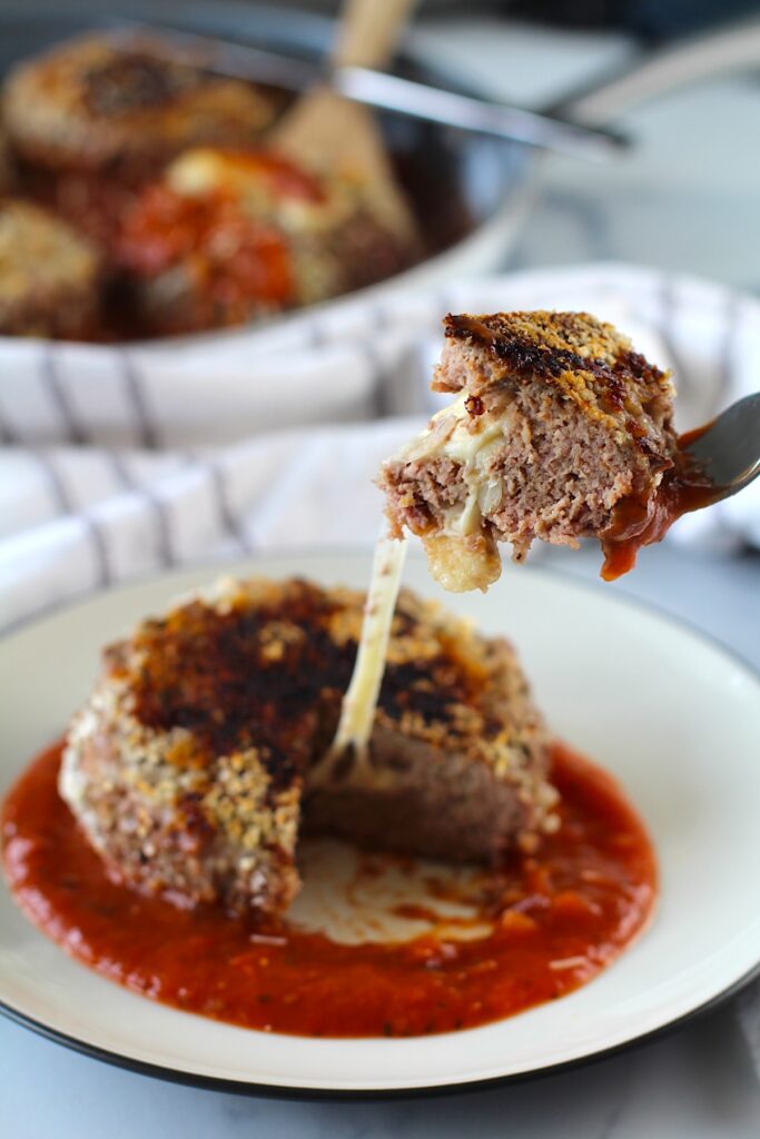 A Ground beef Polpettone sitting on tomato sauce on a plate with a fork pulling a piece up with a long mozzarella cheese pull.